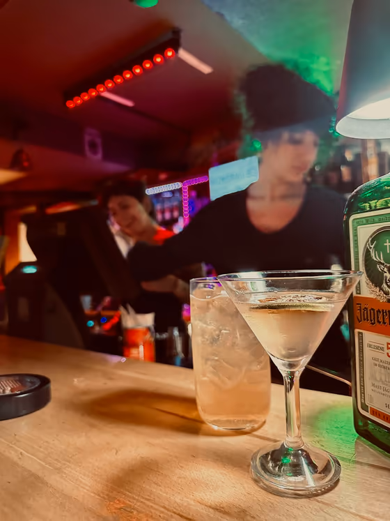 Un cocktail au comptoir, néons du bar en fond